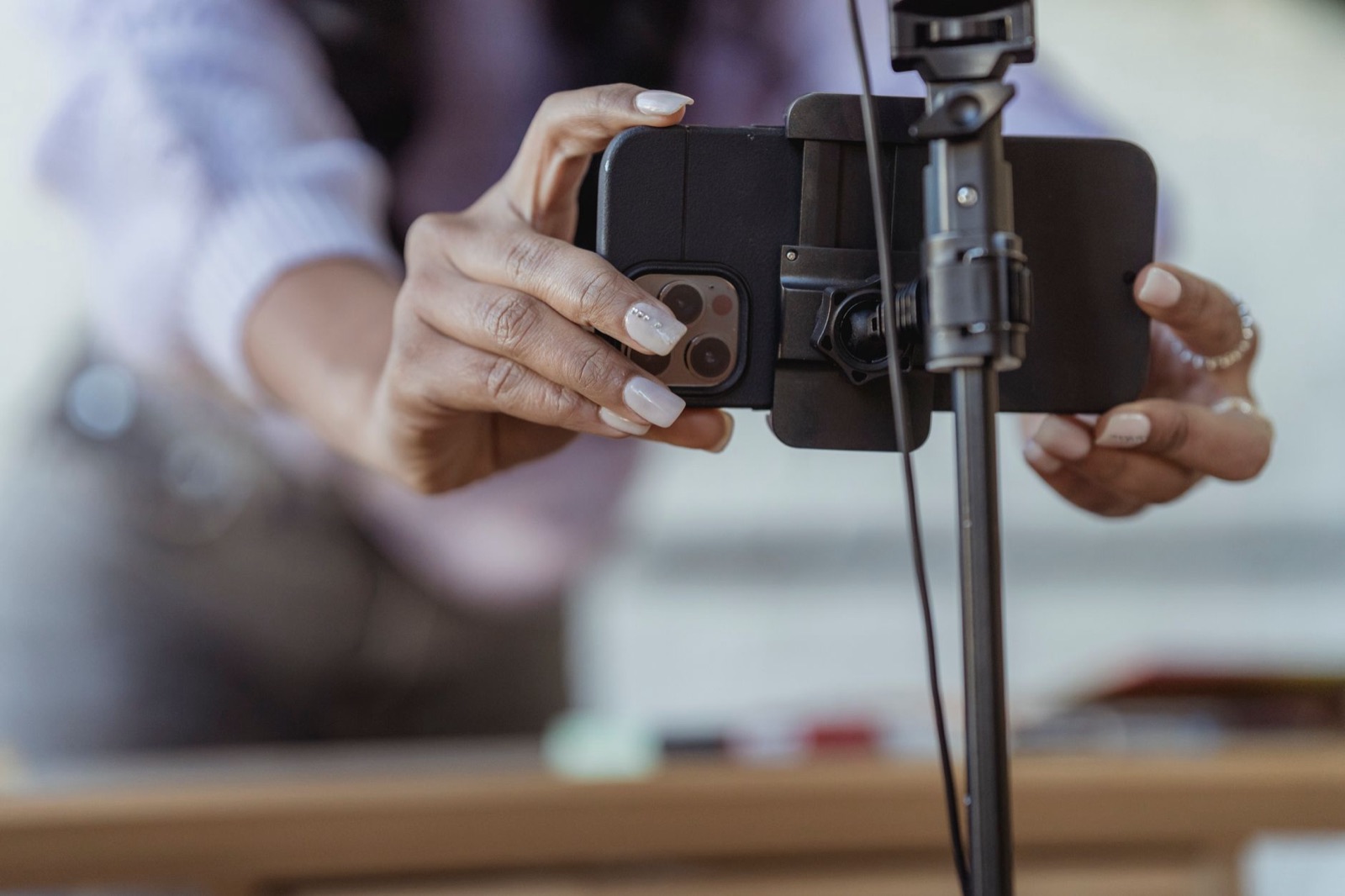 Close-up of a woman's hands clamping a smartphone into a tripod mount, a desk and make-up scattered out of focus behind